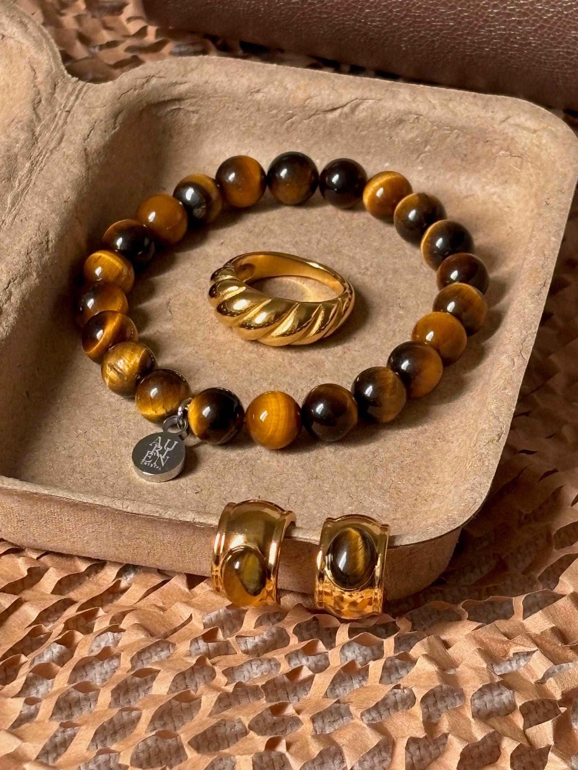 Aurien Crystal yellow Tiger’s Eye bracelet with gold ring and earrings in warm brown flatlay, autumn jewelry styling ideas in neutral color palette, minimalist gemstone accessory set for fall outfits.
