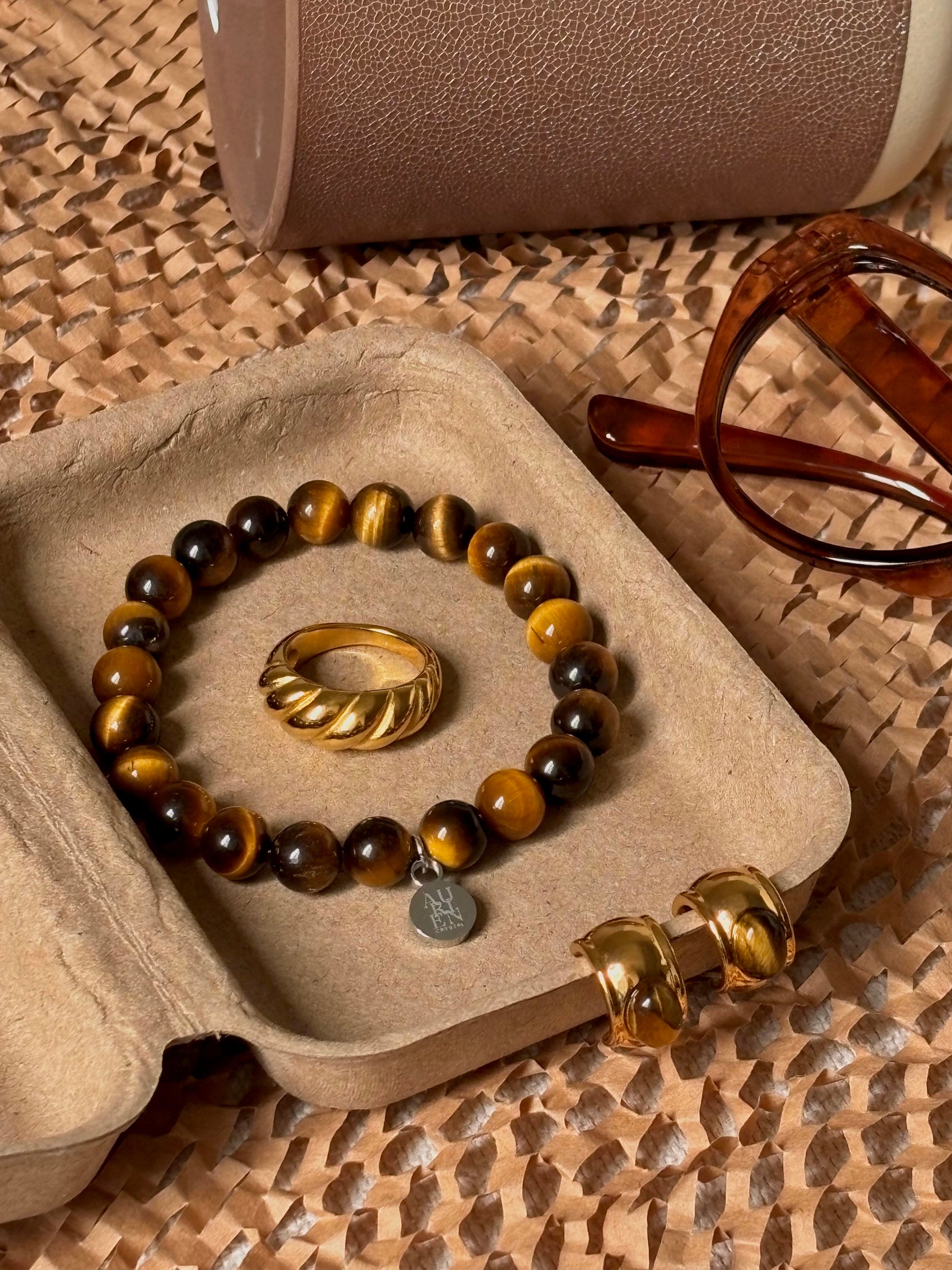 Aurien Crystal golden Tiger’s Eye bracelet with gold ring and earrings in warm brown flatlay, autumn jewelry styling ideas in neutral color palette, minimalist gemstone accessory set for fall outfits.
